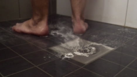 Slightly-defocused-background:-Soapy-water-in-shower-drain,-man's-feet