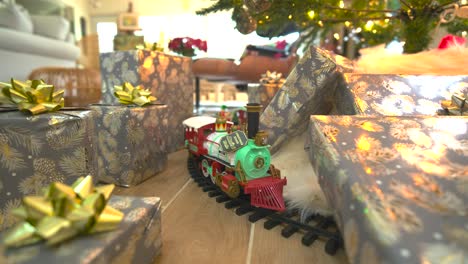 "Captivating-stock-footage:-Glide-beneath-a-festive-Christmas-tree,-presents-galore,-showcasing-a-model-train,-spreading-joy-in-a-delightful-reverse-wide-sliding-shot