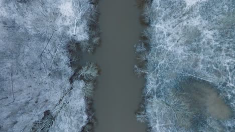 Aerial-birdseye-view-of-valley-of-the-Abava-river-on-overcast-winter-day,-fields-covered-in-snow,-Abava-river-filled-with-dark-flood-water,-wide-drone-shot-moving-forward