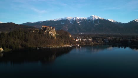 Forward-Drone-Shot-with-Bled-Castle,-Slovenia-and-Julian-Alps-in-Background