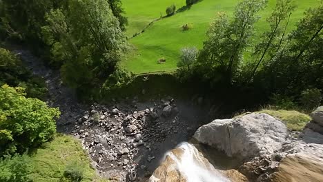 Rasanter-Abstieg-Aus-Der-Luft-über-Einen-Schroffen-Bergwasserfall-Zur-Grünen-Talwiese