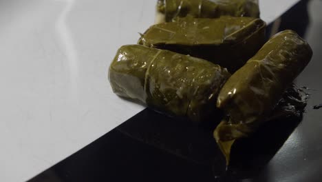 Grape-leaf-wrapped-Dolmades-dripping-in-olive-oil,-placed-onto-platter