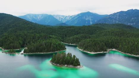 A-beautiful-aerial-view-of-a-turquoise-lake,-lined-with-a-vast-forest-of-trees,-and-majestic-mountain-in-the-background
