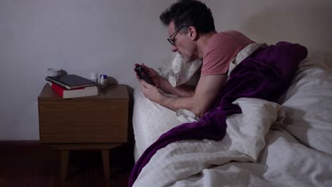 An-adult-man-with-eyeglasses-checking-his-phone-on-bed-and-getting-worry