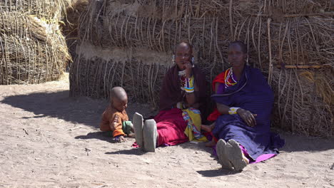 Maasai-Tribe-Women-and-Child-Sitting-on-Ground-By-Hut,-Their-Home-and-Shelter-in-African-Savannah