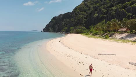 Aerial-drone-shot-a-man-walking-on-a-beach,-at-clear,-blue-water,-on-Black-island,-in-Philippines,-Asia