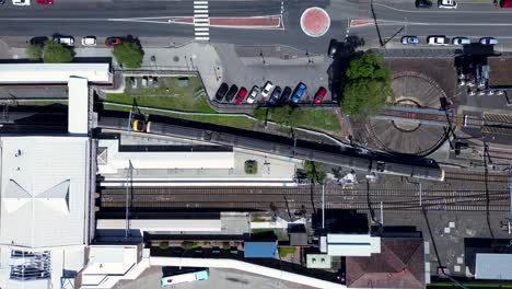Drone-aerial-shot-of-city-rail-train-leaving-Gosford-station-train-tracks-with-carpark-platform-transportation-travel-Central-Coast-Australia-4K