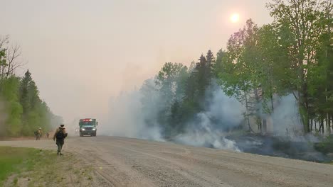 Firefighters-work-on-the-outskirts-of-Alberta-Canada-in-a-wild-forest-fire,-trees-on-fire,-sky-with-smoke