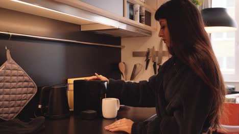 Frau-Im-Bequemen-Bademantel-In-Der-Küche-Benutzt-Maschine,-Um-Eine-Tasse-Kaffee-Zuzubereiten,-Profilansicht