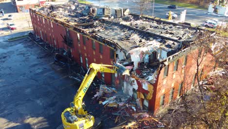 An-excavator-demolishes-a-deteriorated-building-after-forest-fires-in-the-forests-of-Quebec-Canada-Aerial-Drone-Shot