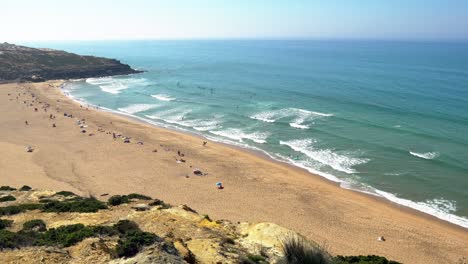 Portugal,-Carvoeira,-Foz-do-Lizandro-beach-from-distance-with-surfers-in-the-water