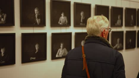 Gray-haired-person-looks-at-row-of-black-and-white-photos-in-art-gallery