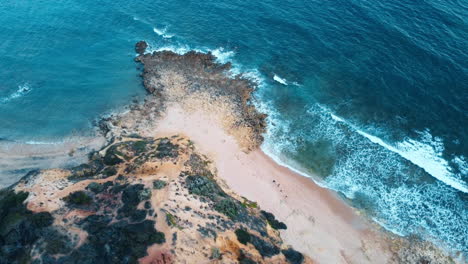 The-aerial-perspective-from-a-bird's-eye-view-captures-Portugal's-rocky-coastline,-showcasing-the-tender-splashes-of-sea-waves-embracing-the-rugged-formations-along-the-coast