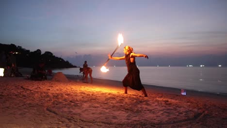 Man-plays-with-spinning-a-fire-stick-during-sunset-on-Haad-Yao-beach,-Koh-Phangan