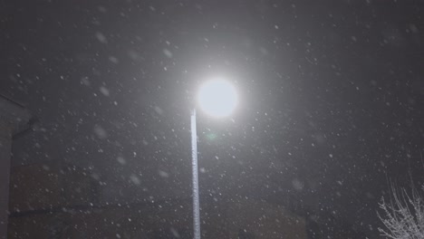 Street-lighting-lamp-around-which-snow-is-falling-at-night-in-the-city