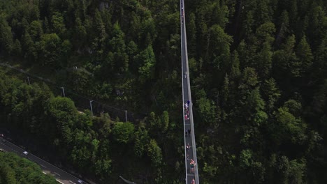 Aerial-view-of-the-world's-longest-pedestrian-suspension-bridge,-connecting-Ehrenberg-Castle-and-Fort-Claudia-in-Austria,-over-a-busy-road-and-surrounded-by-a-forest-of-trees