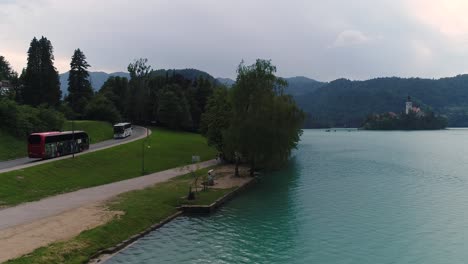 Drone-hovering-view-of-lake-Bled-and-tourists-coming-from-a-bus