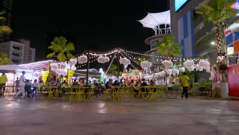 Spätabendskäufer-Kommen-Auf-Einem-Nahegelegenen-Straßenmarkt-Vorbei,-Um-An-Den-Imbissständen-In-Der-Stadt-Bangkok,-Thailand,-Etwas-Zu-Essen-Zu-Kaufen