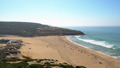 Foz-do-Lizandro-sandy-beach-with-group-of-surfers-in-the-Atlantic-Ocean,-Carvoeira,-Portugal
