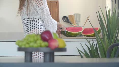 In-the-kitchen,-a-sexy-woman-slices-a-watermelon-with-a-large-knife-in-slow-motion