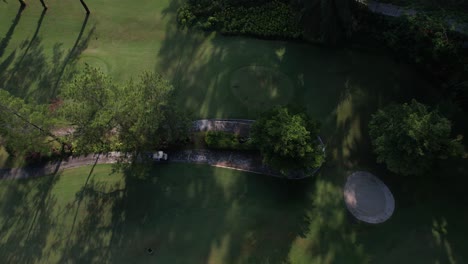 Drone-shot-looks-down,-showing-a-golf-cart-driving-on-the-golf-course