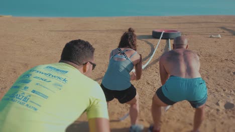 A-Group-Of-athletes-drags-a-huge-car-tire-by-the-beach---Back---Slow-Motion