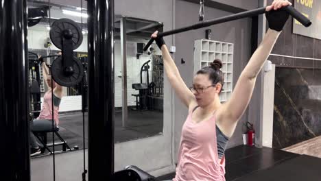 Woman-with-glasses-exercising-with-a-chin-up-machine-in-the-gym,-exercise-movements-for-arm-muscles