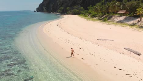 Aerial-orbit-drone-shot-around-guy-walking-on-beautiful-tropical-beach,-on-Black-island,-Philippines,-Asia