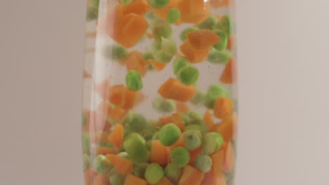 Verduras-Mixtas,-Guisantes-Verdes-Y-Zanahorias-Cayendo-En-Agua-Disparadas-En-4k-Y-Crudas-Con-Estilo-Cine-Sobre-Un-Fondo-Blanco