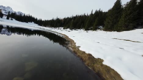 FPV-drone-flying-low-over-ice-and-snow-on-picturesque-alpine-lake,-Italy