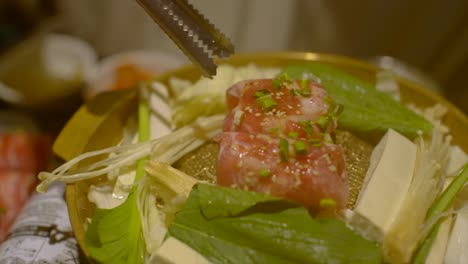 Raw-meat-sprinkled-with-spring-onion-pushed-around-with-tongs-on-Korean-style-BBQ-grill,-filmed-as-slow-motion-close-up-shot