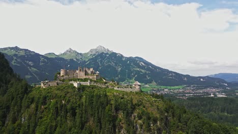 Aerial-view-of-Ehrenberg-Castle-in-Austria,-atop-a-hill,-overlooking-mountains-and-a-town-below,-on-a-cloudy-day