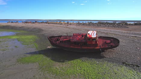 Circular-Drone-Shot-of-a-Wrecked-fishing-boat-which-is-rusted-and-lays-on-the-beach-at-bahia-bustamante
