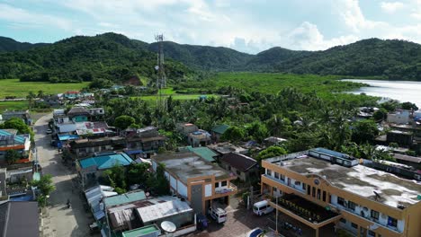 Aerial-dolly-of-picturesque-Filipino-town-center-settlement-with-small-buildings-and-satellite-tower-with-lush-mountains-in-background