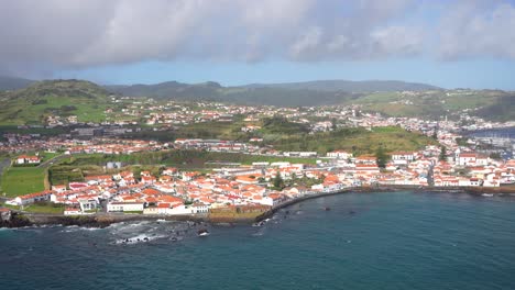 Faial-coastal-city-with-white-buildings,-red-rooftops-and-old-volcanoes-behind