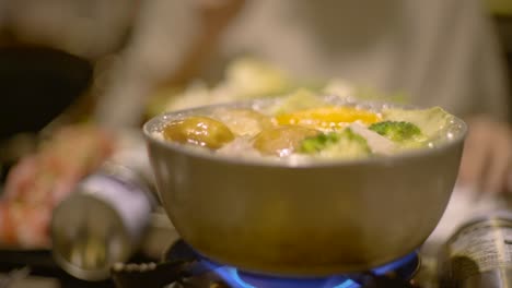 Silver-pot-with-vegetables-boiling-on-gas-stove,-filmed-in-slow-motion-handheld-shot