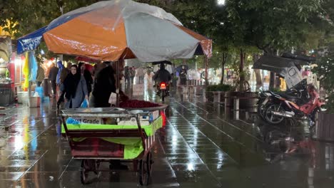 Street-food-grocery-shop-fresh-fruit-selling-on-wheelbarrow-at-night-in-a-rainy-day-Rasht-Gilan-Iran-local-people-farmer-market-in-countryside-rural-area-urban-wide-view-of-cityscape-wonderful-rain