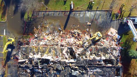 Toma-Aérea-De-Bomberos-Y-Excavadoras-Trabajando-En-Un-Edificio-Destruido-Después-De-Un-Incendio-En-Quebec,-Canadá.