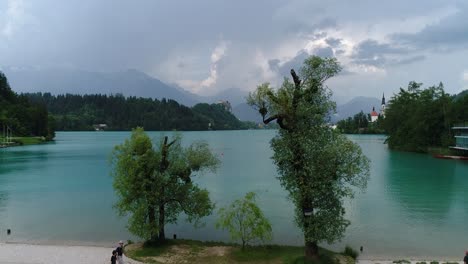 Drone-forward-flying-view-of-Bled-lake-beach-with-people