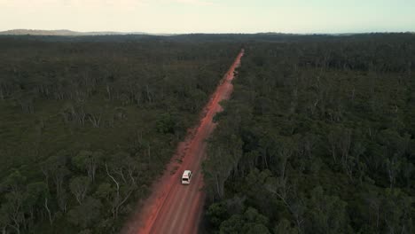 drone-shot-orbiting-around-a-white-van-driving-on-a-asutralian-red-dirt-road-through-the-australian-bush-in-Western-Australia