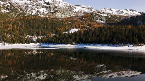 Scenic-winter-mountain-landscape-reflected-in-alpine-lake,-Italian-alps-aerial