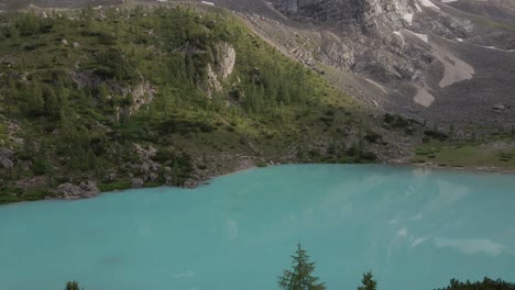 Turquoise-lake-with-pine-trees-filmed-with-a-drone-in-the-mountains-in-the-Italian-Alps,-Dolomites