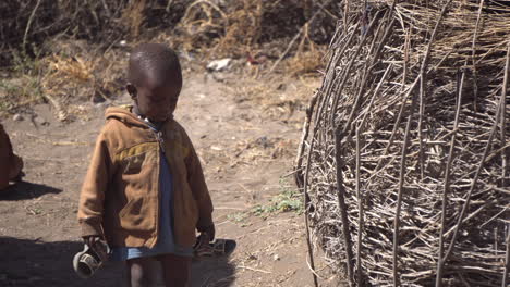 Child-From-Maasai-Tribe-Walking-By-Hut-Shelter-in-African-Savannah,-Tanzania-National-Park