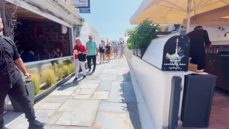 Oia-Santorini-Greece-Island-Travel-Tourist-Immersive-Walk,-Europe,-4K-|-Greek,-Aegean,-Sea,-Cliffside,-Ocean,-City,-Vacation,-Shopping,-White,-Marble,-Crowd,-Flowers,-Traveler,-People,-Couple,-Bar
