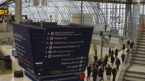 Directional-sign-in-Waterloo-train-station-with-commuters-walking-London-UK