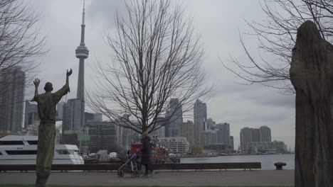 Woman-with-stroller-walks-by-statues-in-foreground-of-Toronto-skyline