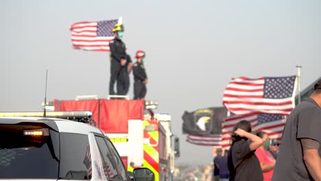 Local-fire-fighters-stand-on-top-of-fire-truck-waiting-for-fallen-solider-to-come-home-during-a-funeral-procession-on-the-highway,-hand-held-shot