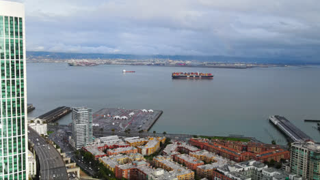 Cinematic-aerial-view-of-a-cargo-ship-carrying-containers-at-Harbour-Bay-San-Francisco-under-cloudy-grey-sky,-CA,-USA