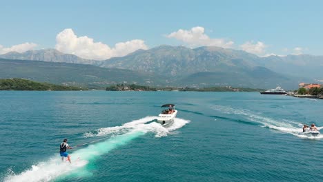 Luftaufnahme-Eines-Schnellboots,-Das-Wasserski-In-Der-Bucht-Von-Kotor,-Montenegro,-Zieht,-Mit-Bergen-Im-Hintergrund