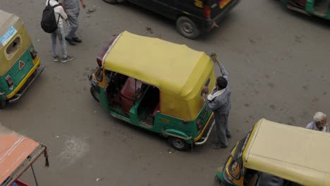 Hombre-Limpiando-Su-Tuk-Tuk-En-Una-Calle-Muy-Transitada,-Delhi,-India